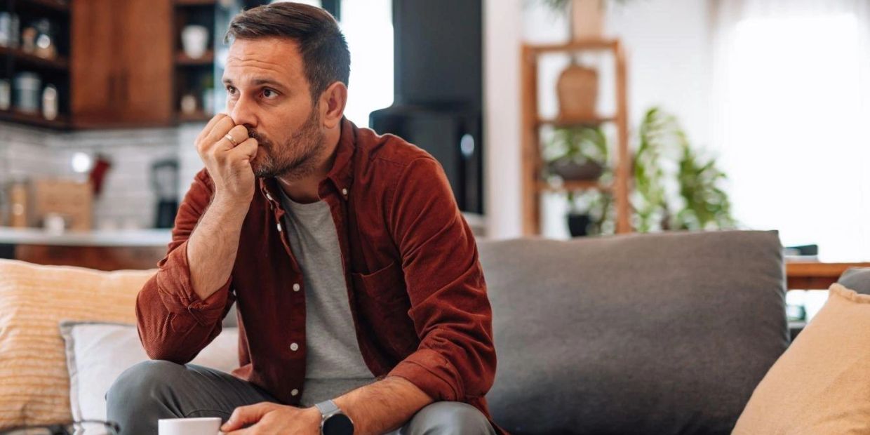 Man sitting with a coffee, lost in thought as his mind races with worry and anxiety