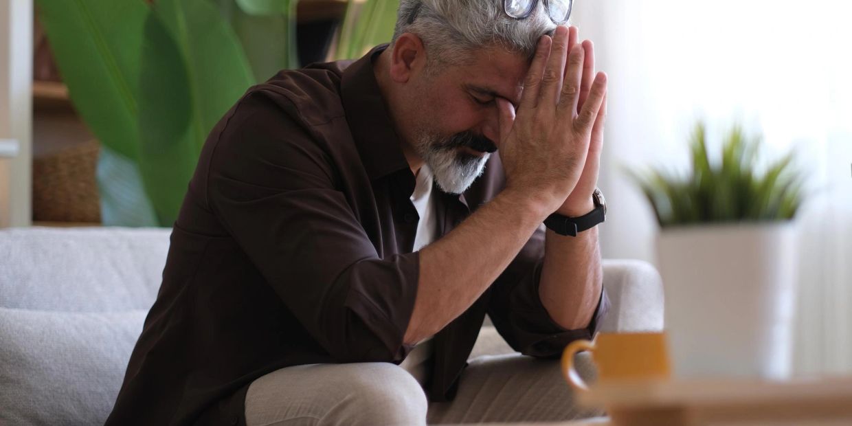 Man sitting alone at home with his head lowered as he experiences a quiet moment of grief