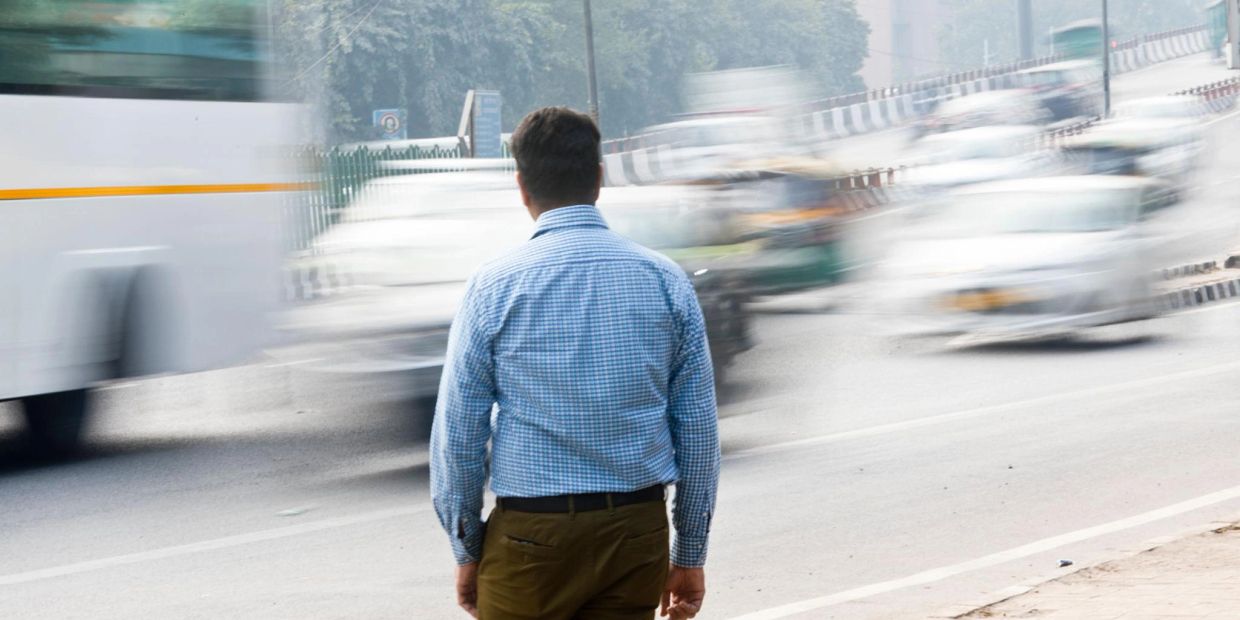 man is standing at the edge of the road with the world passing around him