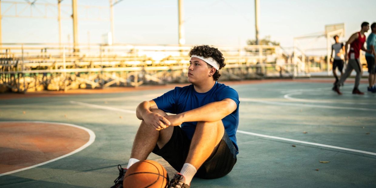 Young man sitting alone on a basketball court, taking a quiet moment to think