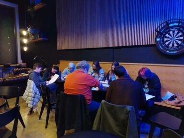 Group of people engaged in a discussion around a table in a dimly lit room.