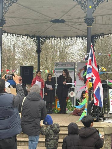 People gathered at an outdoor event with speakers and flags on a stage.
