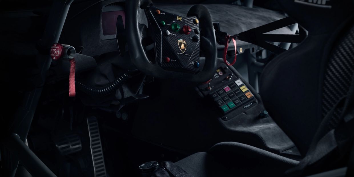 Dark interior of a Lamborghini race car with a detailed steering wheel and control panel.