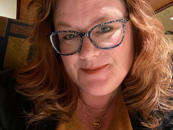 Smiling woman with curly hair and patterned glasses.