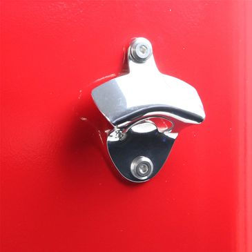 Shiny metal bottle opener mounted on a bright red surface.