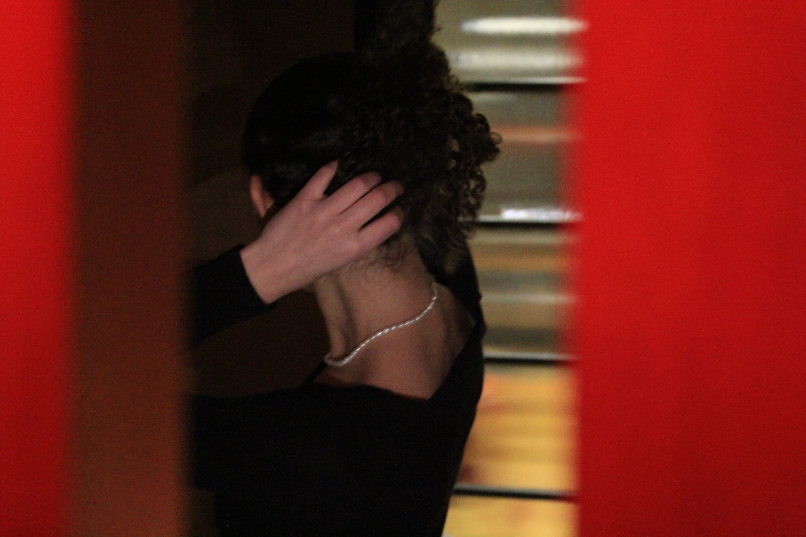 Person with hand on head and curly hair, viewed from behind.