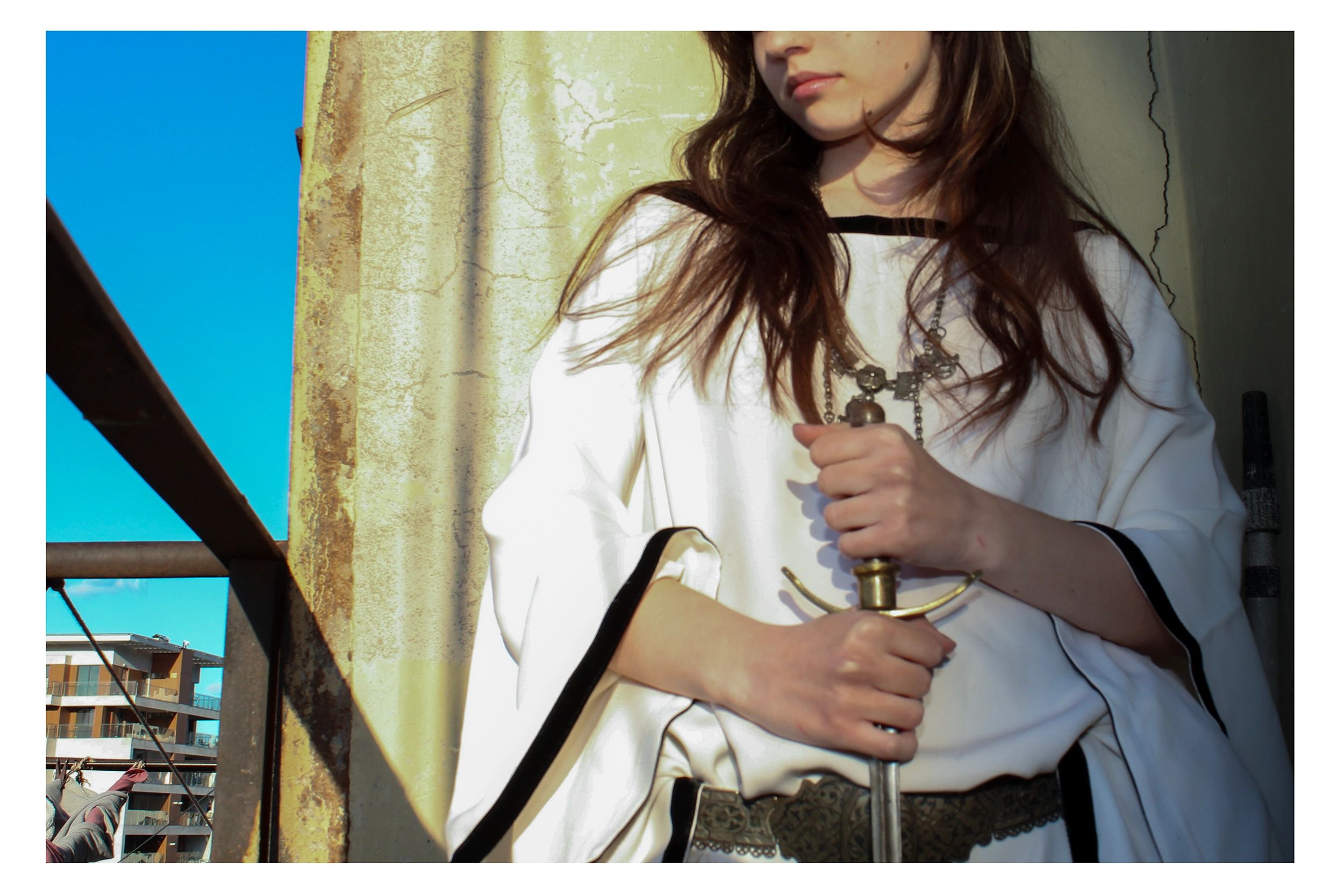 Person in white holding a sword with urban background.