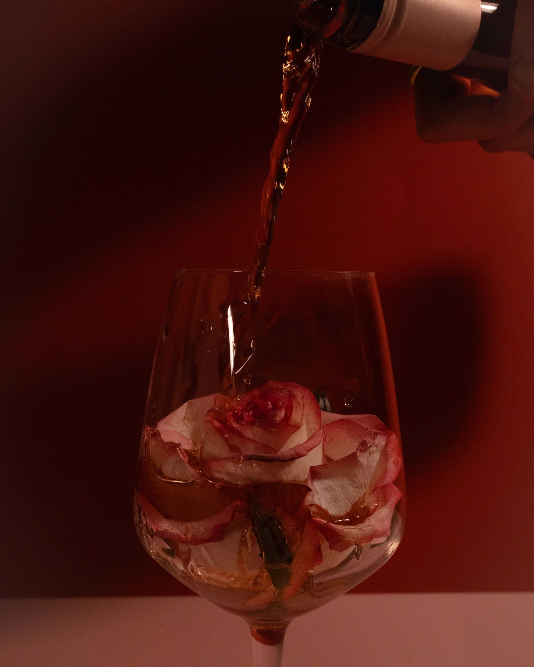 Liquid being poured over a rose in a glass.