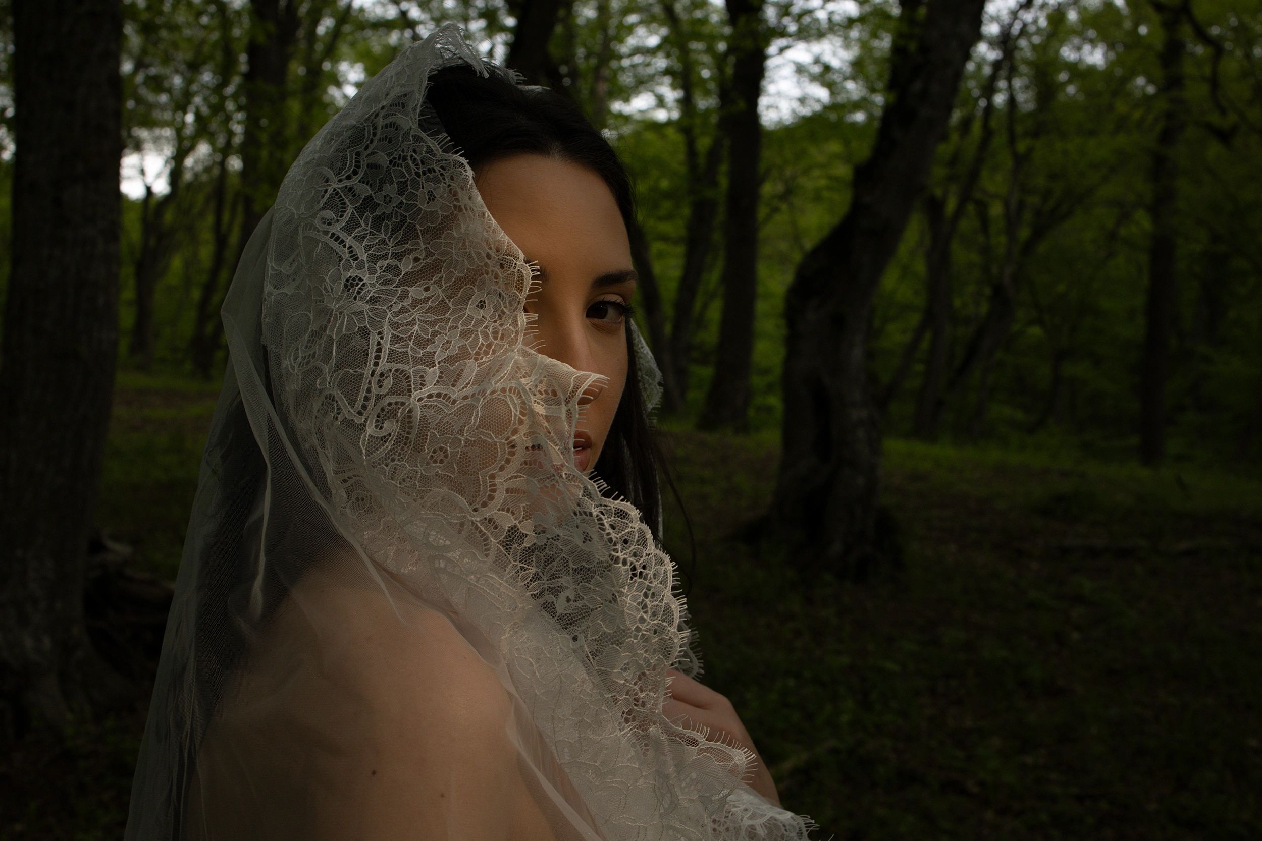 Woman in lace veil in a forest setting.