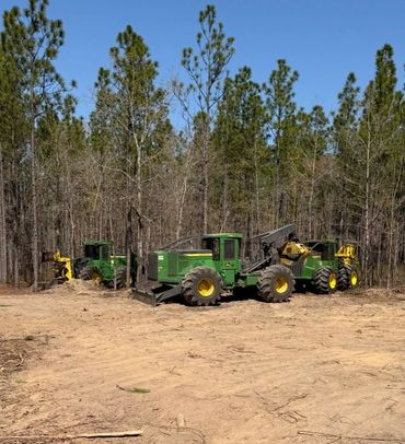 Three green forestry machines parked near a wooded area under clear blue sky.
