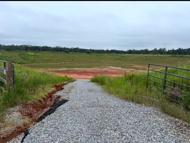 Gravel pathway leading to a fenced, grassy depression under a cloudy sky.