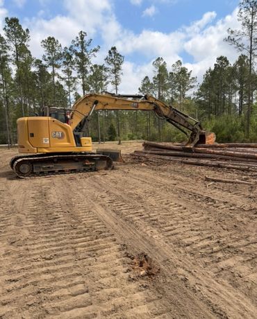 A yellow CAT excavator near stacked logs in a forest clearing.