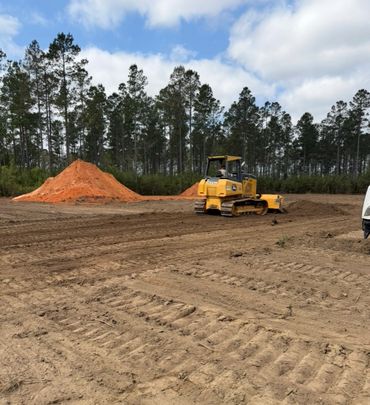 A yellow bulldozer leveling a dirt area with trees in the background.