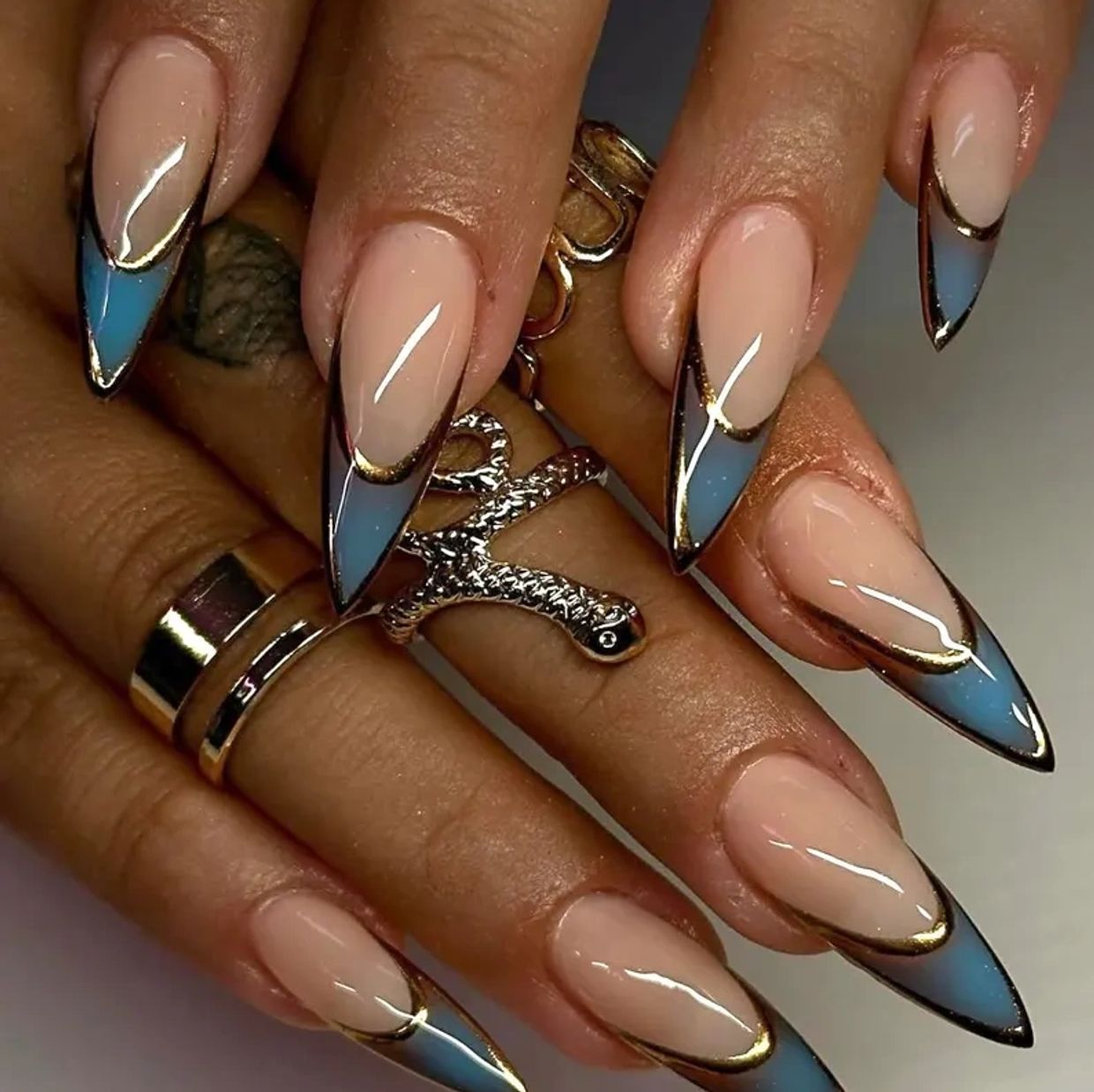 Long almond-shaped nails with nude, blue, and gold trim design.