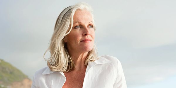 Confident mature woman in white shirt gazing thoughtfully outdoors.