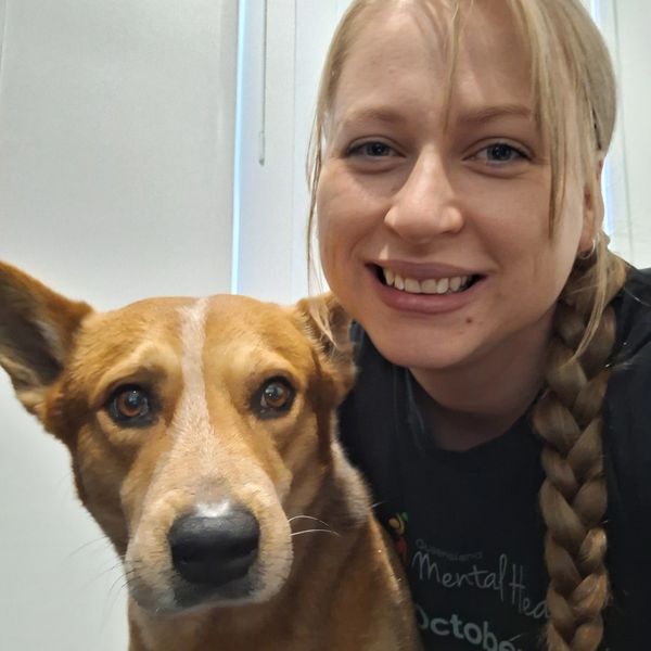 Smiling woman with long braid posing closely with a brown dog.