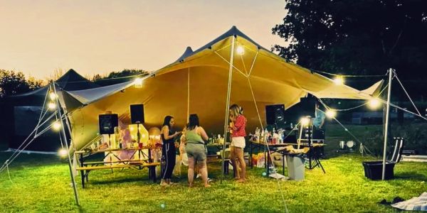 Outdoor party under a tent with lights and people.