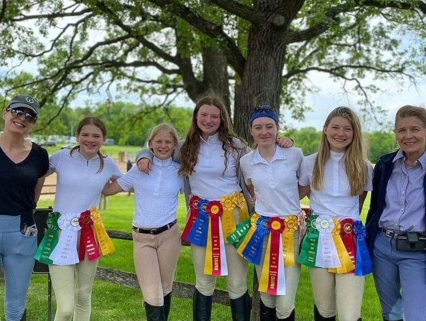 5 horse riders and 2 trainers standing taking a photo after event 