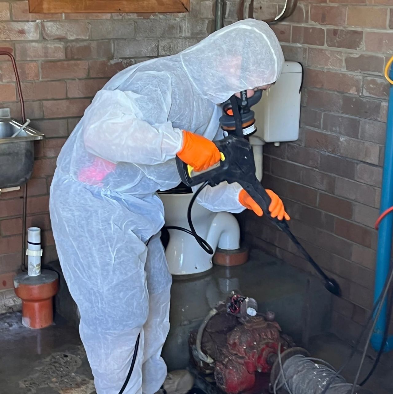 Restoration worker in protective suit cleaning flooded basement with pressure washer. Restoration worker in protective suit cleaning flooded basement with pressure washer.