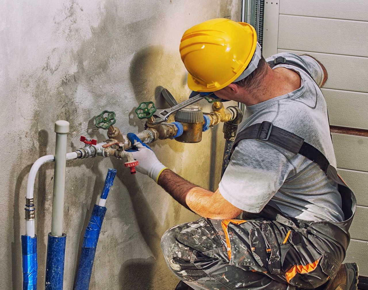 Plumber in hard hat repairing leaking water pipes on wall. Plumber in hard hat repairing leaking water pipes on wall.