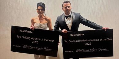 Two individuals holding awards for top real estate achievements in 2025.