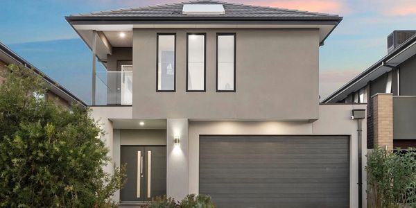 Modern two-story house with a balcony and a double garage at sunset.