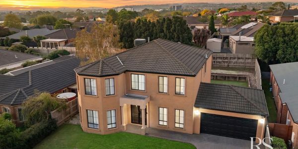 A large two-story house with a black roof at sunset.