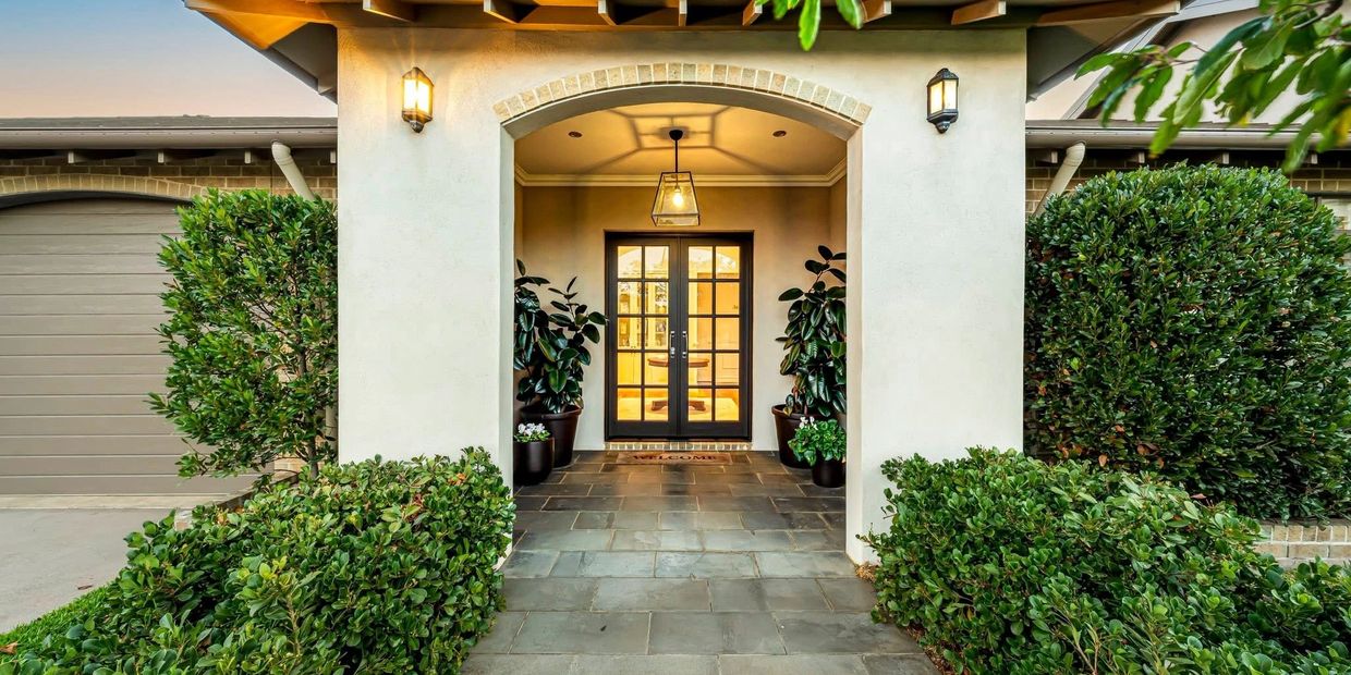 Elegant front entrance with double glass doors and lush greenery.