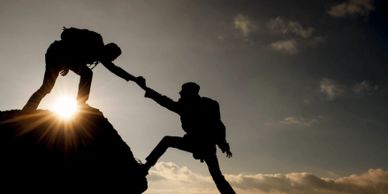 Two people climbing a mountain, one helping the other up.