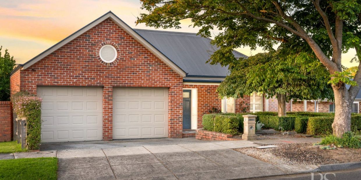 Brick house with double garage and lush greenery at sunset.