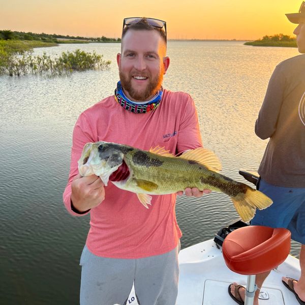 Man proudly holds a largemouth bass on a boat at sunset.
