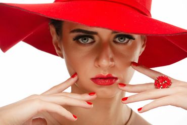 Woman in red hat and matching lipstick and nails poses intensely.