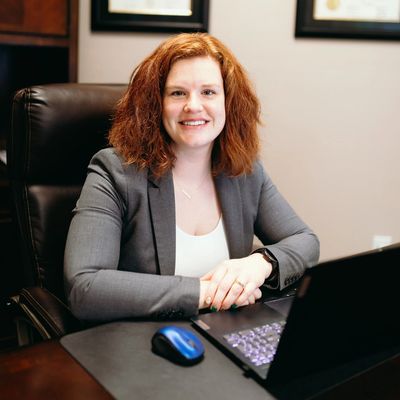 Smiling woman in business attire sitting at a desk with a laptop.