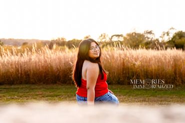 Young woman in red top sitting outdoors with tall grass.