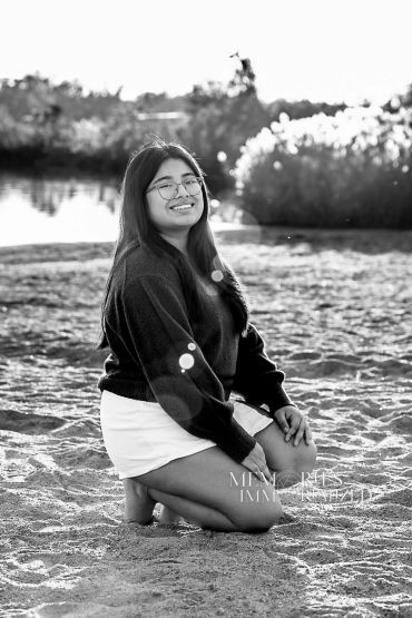 Young woman kneeling on sandy shore with a bright smile.