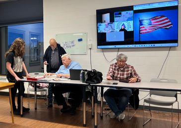 Four people engaged in a meeting room with a screen displaying the American flag.