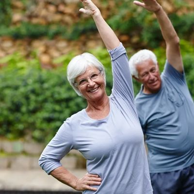 Older couple exercising outdoors, smiling and stretching their arms.