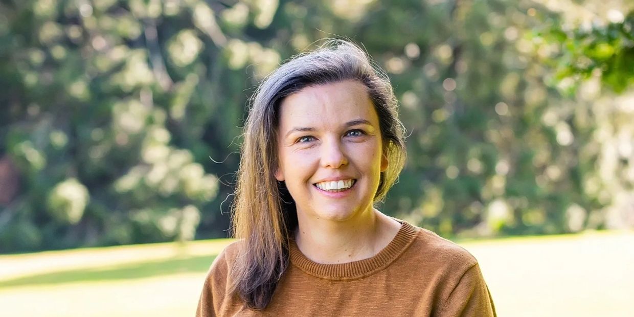 Smiling woman outdoors in a brown sweater with green blurred background.