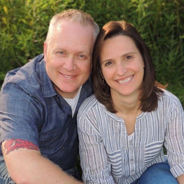 Smiling couple sitting outdoors against greenery, enjoying a sunny day.