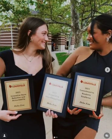 Two women smiling, holding awards from University of Louisville.