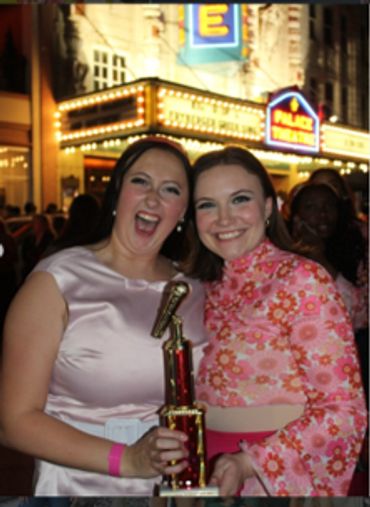 Two women smiling and holding a trophy outside at night.
