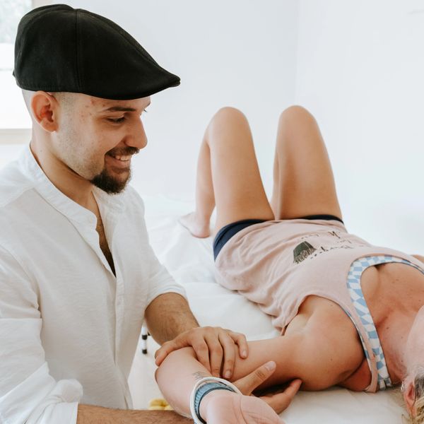 A man in a cap smiling while holding a woman's arm on a bed.