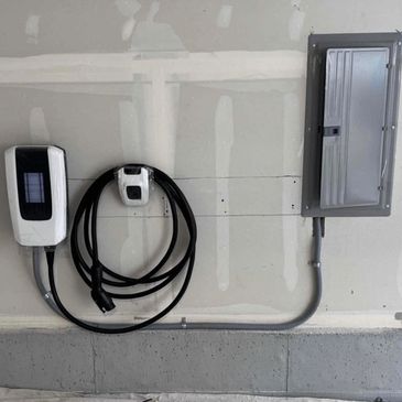 Electric vehicle charging station mounted on a garage wall next to an electrical panel.