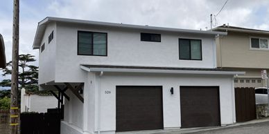 Modern white house with dark brown garage doors on a sloped street.
