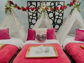 Three indoor teepees decorated for a sleepover party with pink and white bedding, pink blankets, and