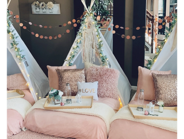 Three indoor teepees are set up for a sleepover party. The teepees are decorated with pink and white