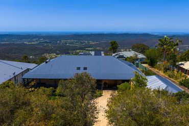 House with metal roof overlooking vast green hills and distant city skyline.