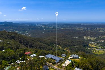 Aerial view of a residential area with a location marker and vast greenery under a clear blue sky.