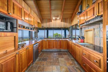 Spacious wooden kitchen with large windows and stone tile flooring.