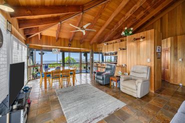 Cozy living room with wooden walls, ceiling beams, and large windows overlooking a scenic view.